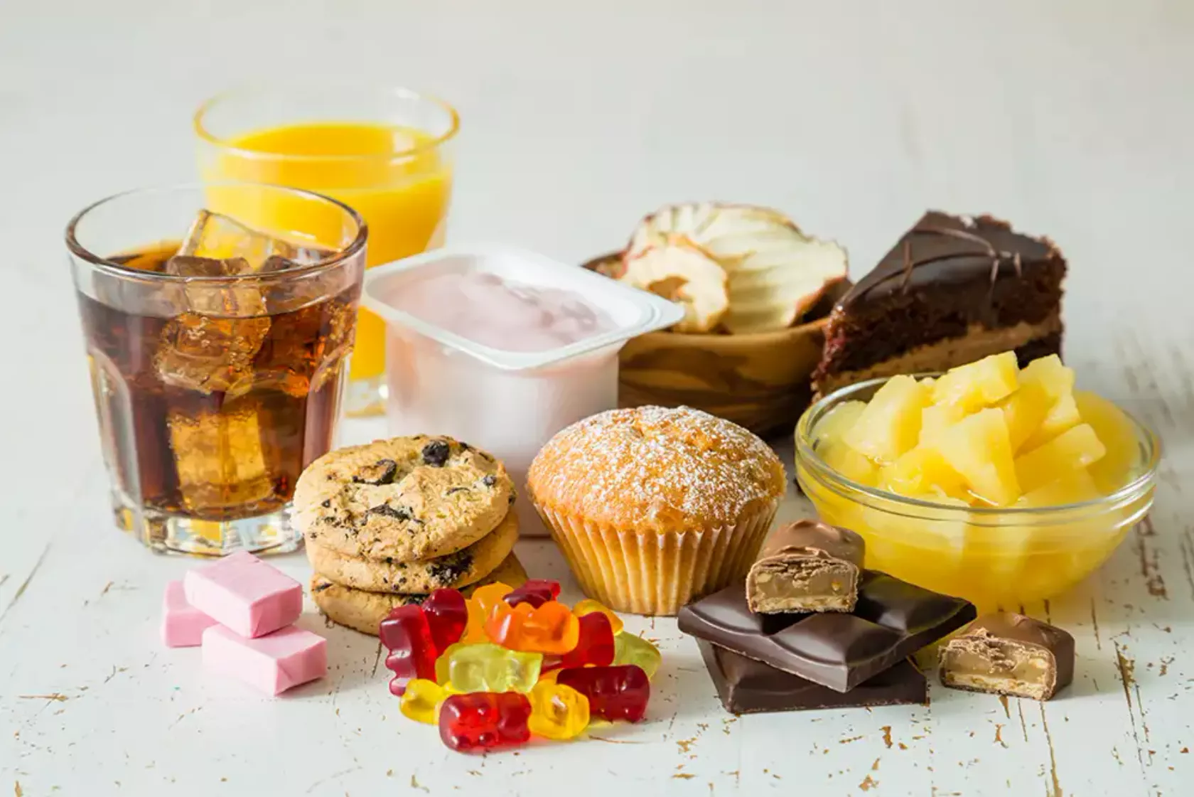 Anordnung von stark zuckerhaltigen Lebensmitteln wie Gummibärchen, Kuchen, Dosenobst, Limonade, Schokolade.