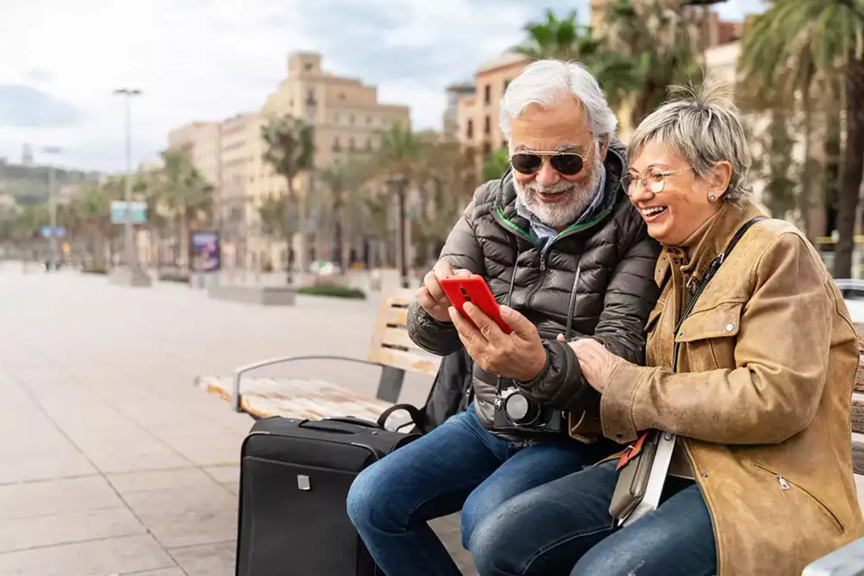 Älteres Paar in Urlaubsland lacht und schaut aufs Handy.