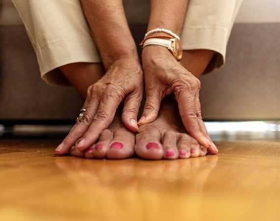 Füße einer Seniorin mit lackierten Nägeln, sie hält sie mit den Händen.