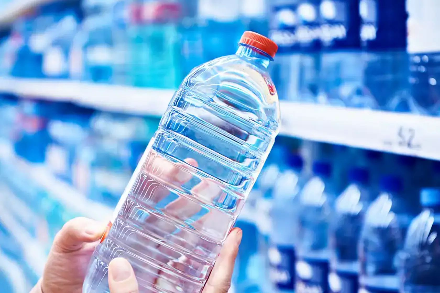 Regal voller Plastik-Wasserflaschen im Supermarkt und eine Frau hält eine Flasche hoch.
