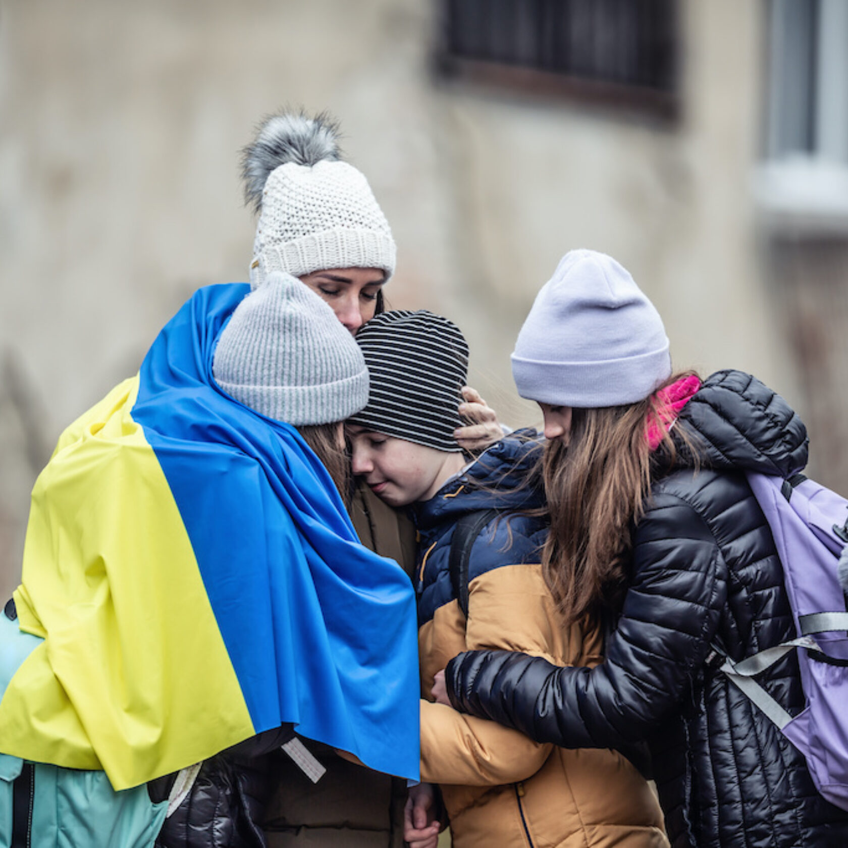 vier Jugendliche und Kinder umarmen sich und tragen die Ukrainische Flagge um die Schultern