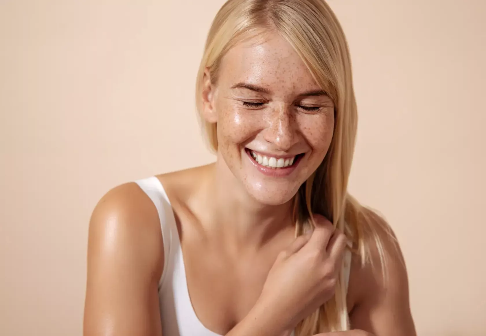 Eine blonde junge Frau mit vielen Sommersproßen lacht in die Kamera. 