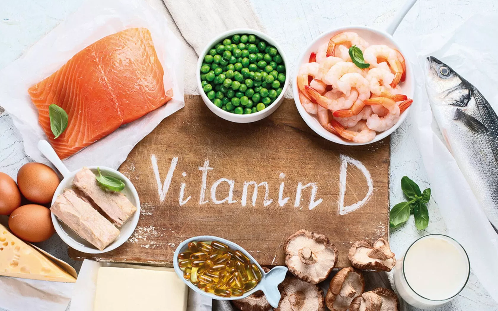 Schriftzug Vitamin D umringt von Vitamin-D-haltigen Lebensmitteln wie Lachs Eier Erbsen Garnelen Fisch